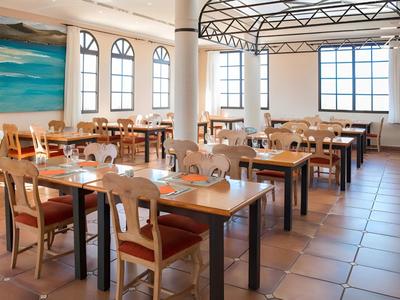 Bright hotel restaurant with wooden tables, chairs, and large windows.