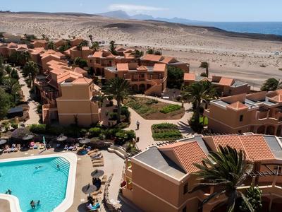 Hotel complex with multiple buildings, pool, and view of desert landscape and sea.