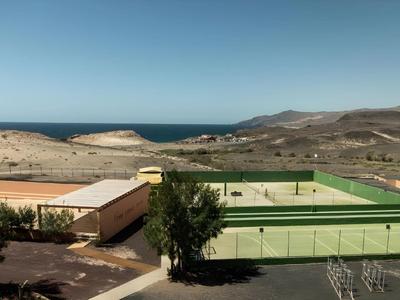 Zelený tenisový kurt před pouštní krajinou s horami a modrou oblohou.