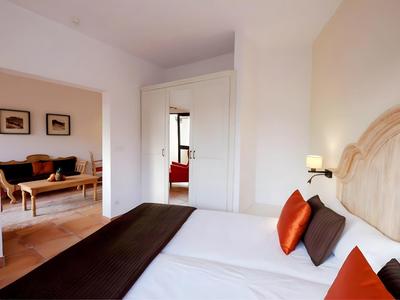 Brightly furnished hotel room with a large bed and adjacent living room.