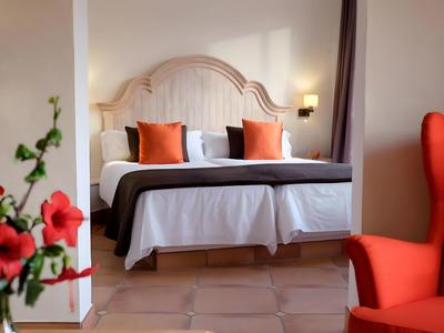 Bright hotel room with comfortable double bed, red accents, and cozy armchair.