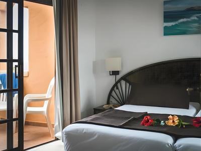 Cozy hotel room with bed, wall lamp, and balcony with chair and table.