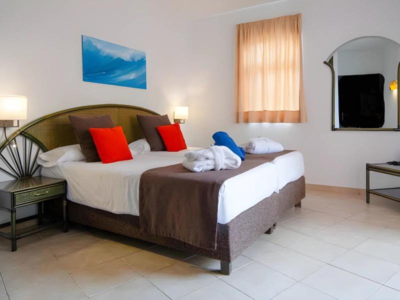Bright hotel room with double bed, red pillows, and decorative wall art.
