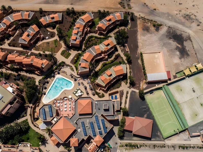 Aerial view of a resort with pools and buildings next to a sandy area.