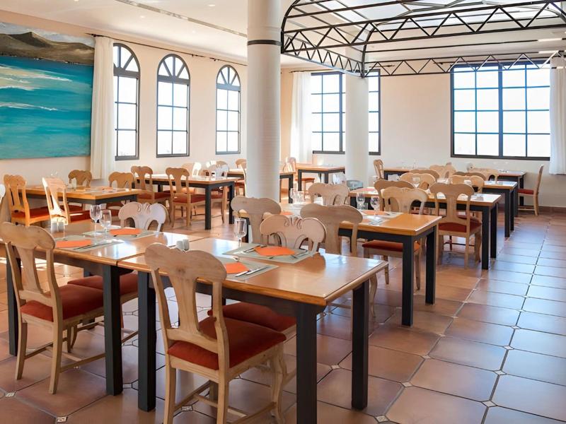 Bright hotel restaurant with wooden tables, chairs, and large windows.