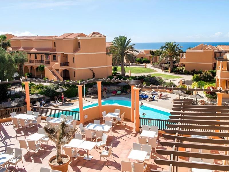 Hotel with swimming pool, terrace furniture, and sea view under clear sky.