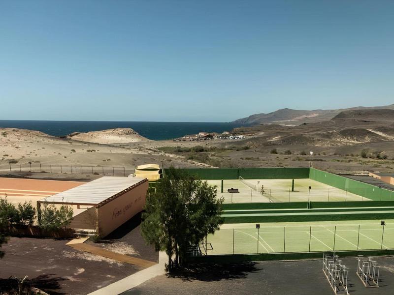 Green sports field in a dry, mountainous landscape overlooking the sea.
