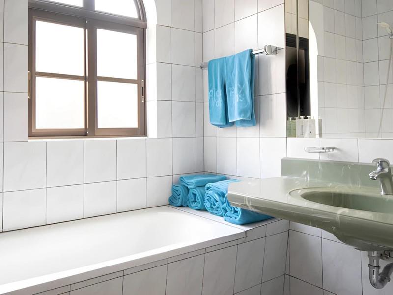 Bright bathroom with white tiled walls, bathtub, green sink, and blue towels.