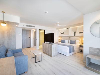 Camera d'hotel luminosa con letto matrimoniale, divano, TV e design moderno.