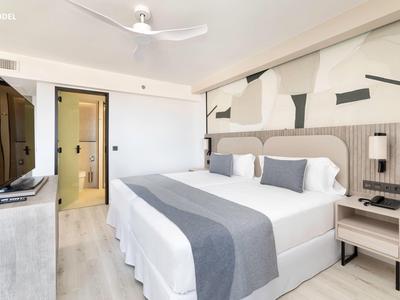Camera d'hotel moderna con letto matrimoniale, tonalità di grigio e arredi minimalisti.