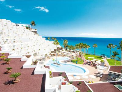 Hotel mit weißer terrassenförmiger Architektur, Pool und Meerblick unter blauem Himmel.
