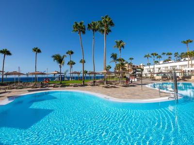 Großer Außenpool in einem Resort mit Palmen und klarem blauem Himmel.