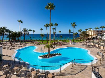 Großer Hotelpool mit Palmen und Blick auf das Meer unter klarem Himmel.