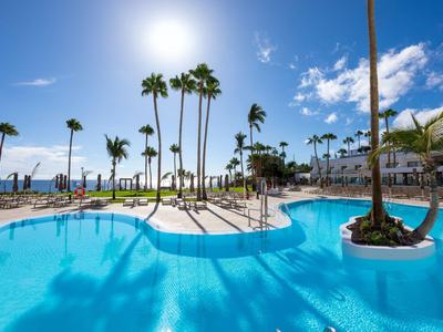 Kräftiger blauer Hotelpool mit Palmen und klar blauem Himmel im Hintergrund.