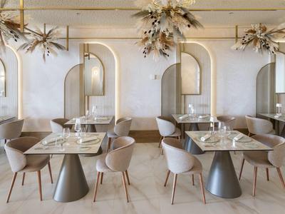 Ristorante moderno con sedie grigie, tavoli in marmo e specchi decorativi alle pareti.