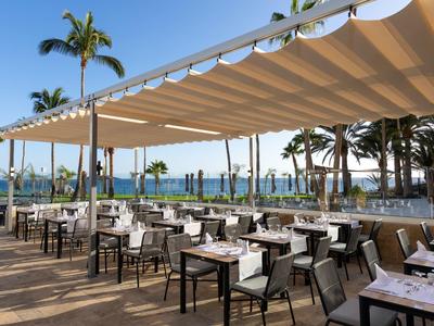 Area esterna di un ristorante con tavoli sotto una tenda e vista sul mare.