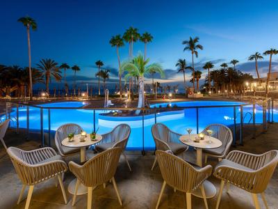 Beleuchteter Hotelpool mit Palmen und Sitzbereichen bei Abenddämmerung.