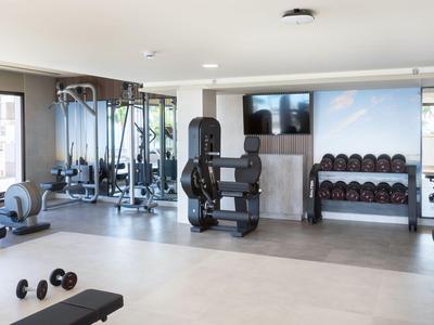 Heller Fitnessraum mit modernen Geräten, Hanteln und großen Fenstern mit Stadtblick.