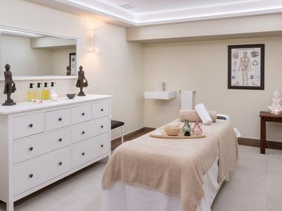Ein schlichter Wellnessraum mit Massageliege, weißen Schränken und beruhigender Beleuchtung.