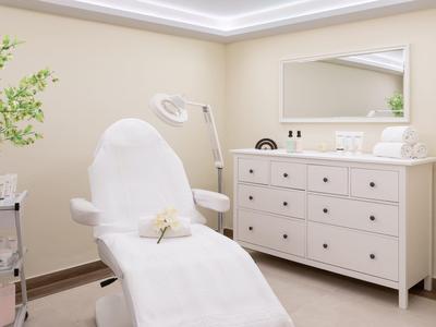 Camera per trattamenti luminosa con poltrona, comò e pianta decorativa per benessere e bellezza.