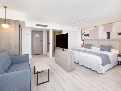 Helles Hotelzimmer mit großem Doppelbett, blauem Sofa und moderner Einrichtung.