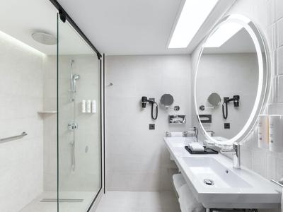 Modernes Badezimmer mit großer Dusche, großem Spiegel und weißem Waschbecken in Hotelzimmer.