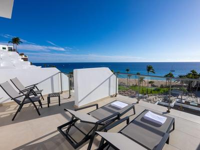 Terrasse mit Liegestühlen und Stühlen mit Meerblick und klarem Himmel.