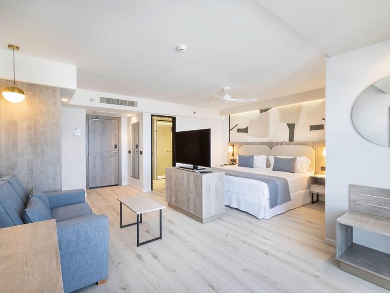 Camera d'hotel luminosa con letto matrimoniale, divano, TV e design moderno.