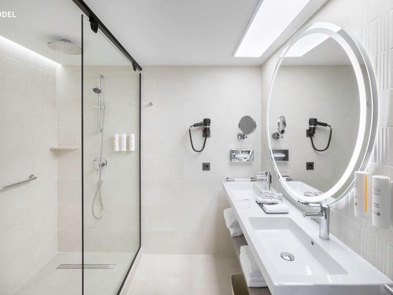 Bagno moderno con grande specchio rotondo illuminato, doppi lavandini e doccia.