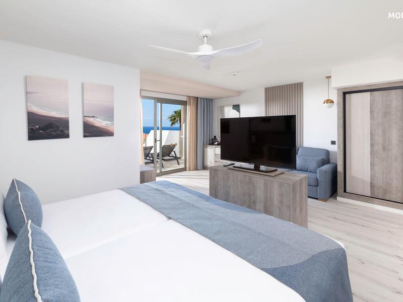 Camera d'hotel luminosa con letto matrimoniale, TV, balcone e vista mare.