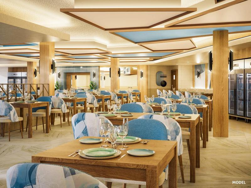 Ampia sala ristorante con tavoli in legno, sedie blu e illuminazione moderna a soffitto.