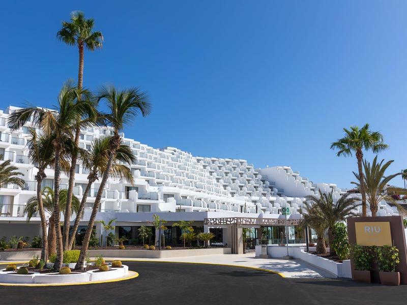 Edificio alberghiero bianco moderno con palme e cielo azzurro limpido sullo sfondo.