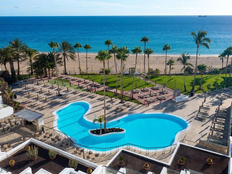 Vista su una piscina dell'hotel con lettini, palme e spiaggia vicino al mare.