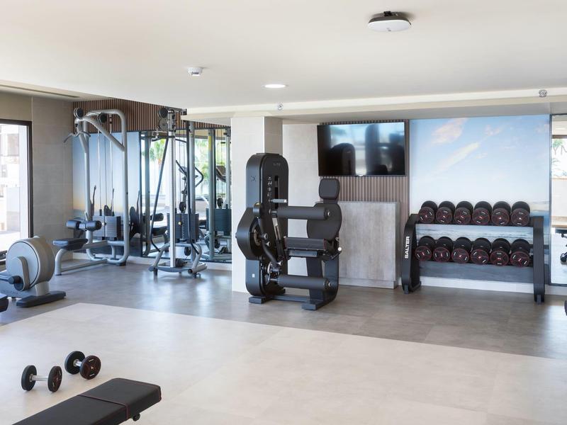 Palestra moderna con attrezzature per allenamento, manubri e grandi finestre che fanno entrare la luce naturale.