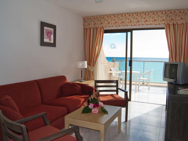 Soggiorno con divano rosso, sedie, tavolo e vista sul mare attraverso una grande porta scorrevole in vetro.