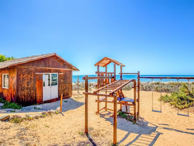 Capanna di legno accanto a un'area giochi sulla spiaggia sotto un cielo azzurro