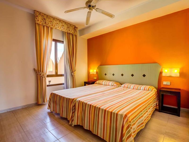 Camera d'hotel luminosa con letto matrimoniale, parete arancione e ventilatore a soffitto