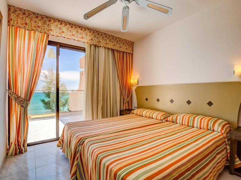 Camera luminosa con due letti, ventilatore a soffitto e porta patio con vista sulla piscina.