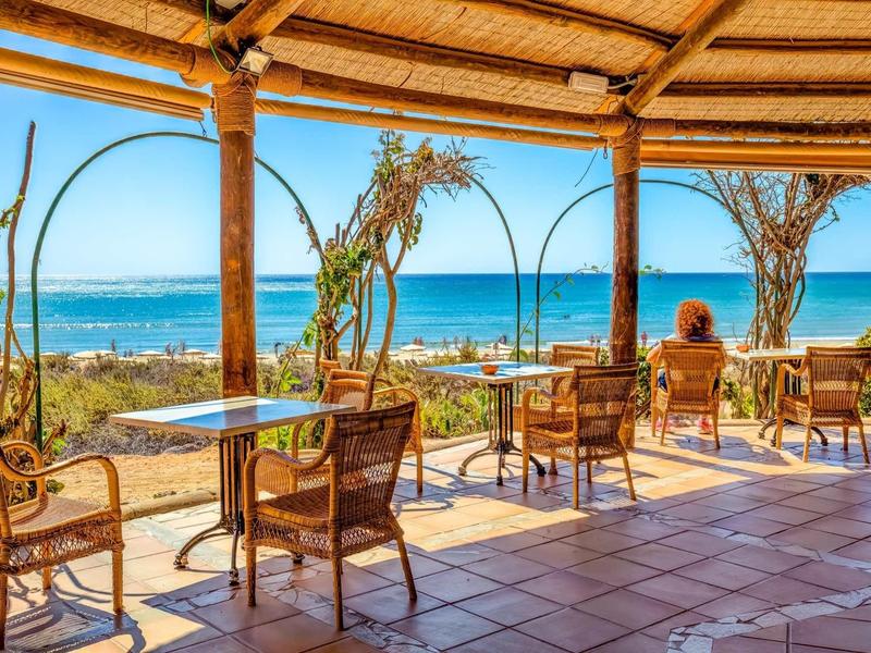 Terrazza aperta con sedie di vimini e tavoli con vista sul mare e sul cielo blu.
