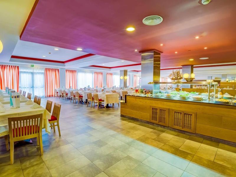 Ristorante luminoso con sedie in legno, tavoli e un'area buffet con piatti caldi.