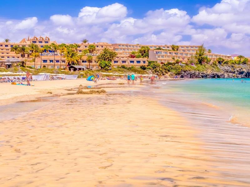 Una spiaggia soleggiata con acqua limpida e un hotel sullo sfondo.