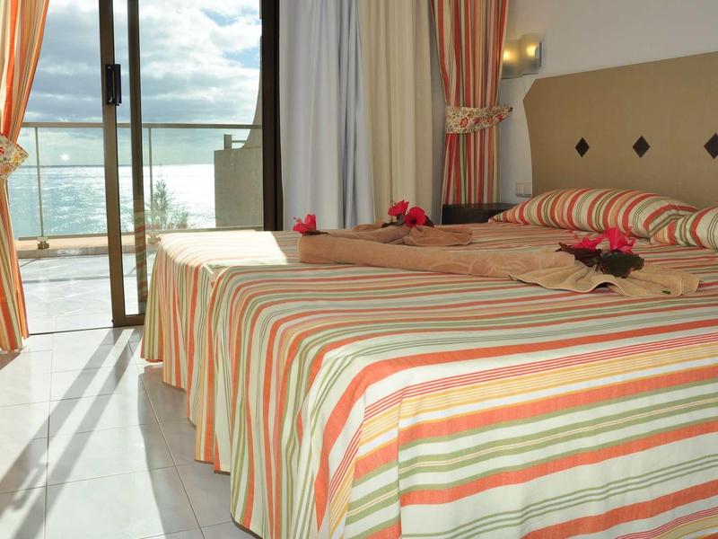 Camera d'hotel con due letti, coperte a righe e vista sul mare dal balcone.