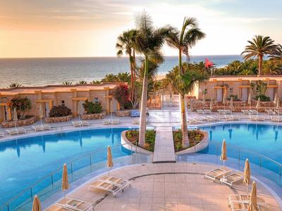 Runder Hotelpool mit Palmen und Meerblick bei Sonnenuntergang.