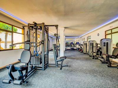 Großer Fitnessraum mit modernen Trainingsgeräten und Teppichboden in einem Hotel.