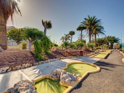 Minigolfanlage mit grünen Bahnen, Palmen und steiniger Umrandung unter blauem Himmel.