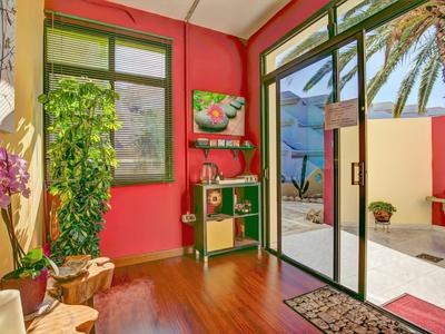 Hell eingerichteter Raum mit roten Wänden, Pflanzen und Blick auf Terrasse mit Blick aufs Meer.