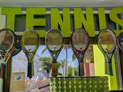 Bunte Tennisschläger hängen vor einem Fenster mit dem Schriftzug TENNIS darüber.