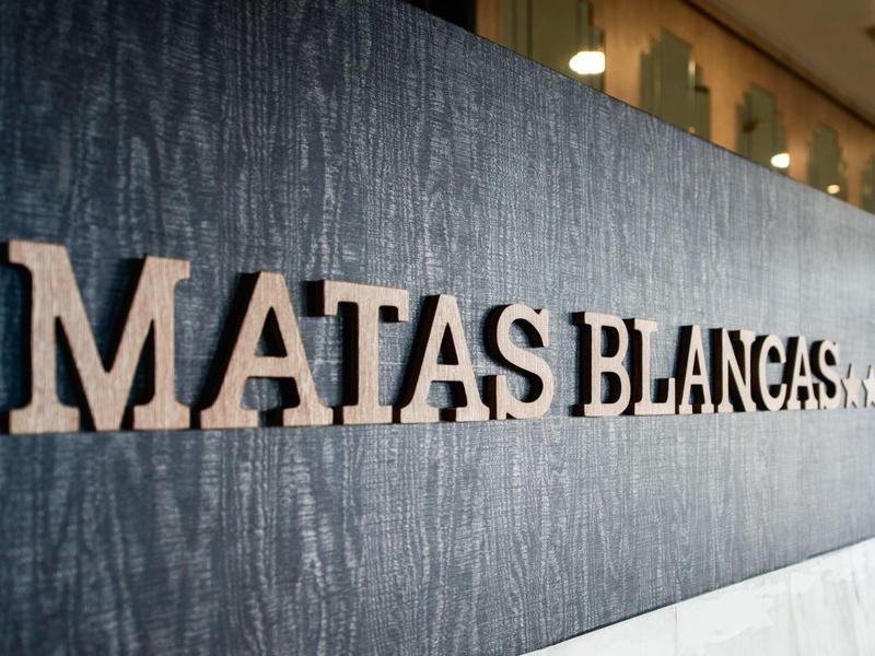 Lettere di legno con scritto 'MATAS BLANCAS' su una parete scura e strutturata.