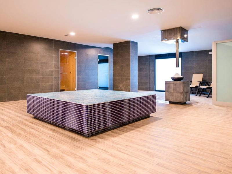 Ampia stanza moderna con grande letto quadrato, pavimenti in legno e zona salotto.