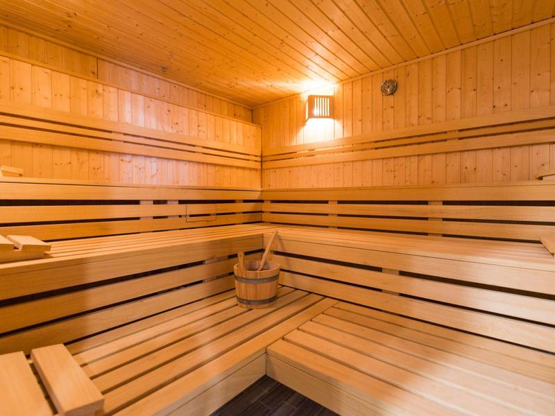 Sauna accogliente in legno con panchine, secchio e mestolo sotto luce calda.